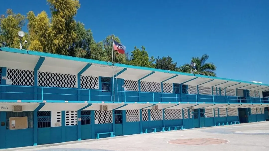 Le long bâtiment bleu à étage du Collège Immaculée Conception des Gonaïves, drapeau haïtien au vent.