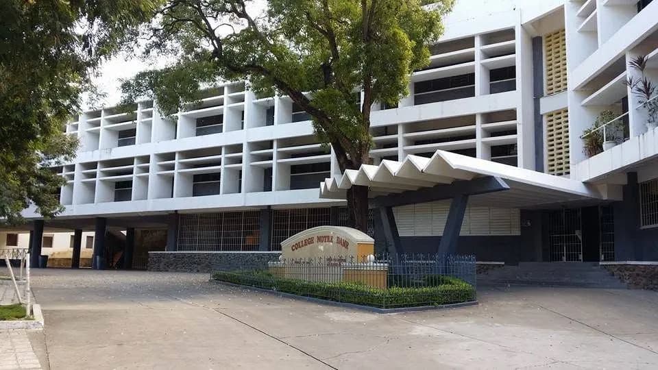 La façade blanche du Collège Notre-Dame du Perpétuel Secours et son entrée sous un grand arbre.